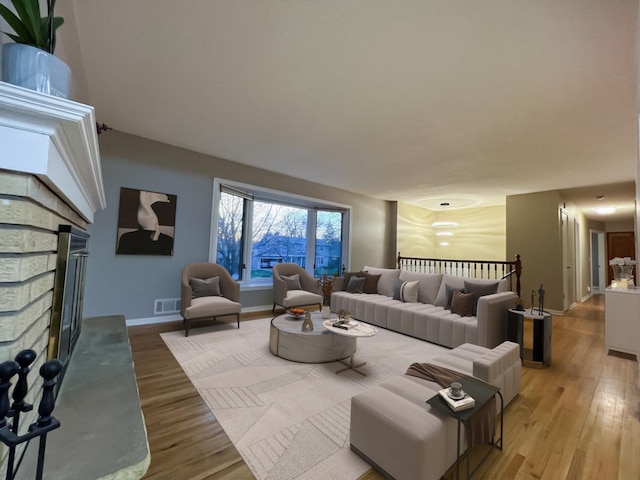 living area with light wood-style floors, baseboards, visible vents, and a stone fireplace