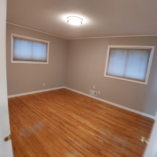 spare room featuring a textured ceiling, visible vents, baseboards, and light wood-style floors