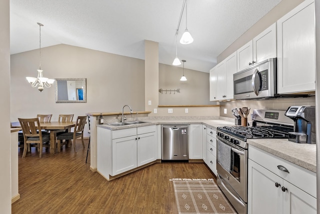 kitchen with lofted ceiling, a sink, a peninsula, a chandelier, and stainless steel appliances