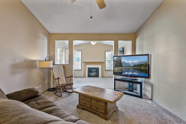 living room with carpet flooring, a ceiling fan, a textured ceiling, and a tile fireplace