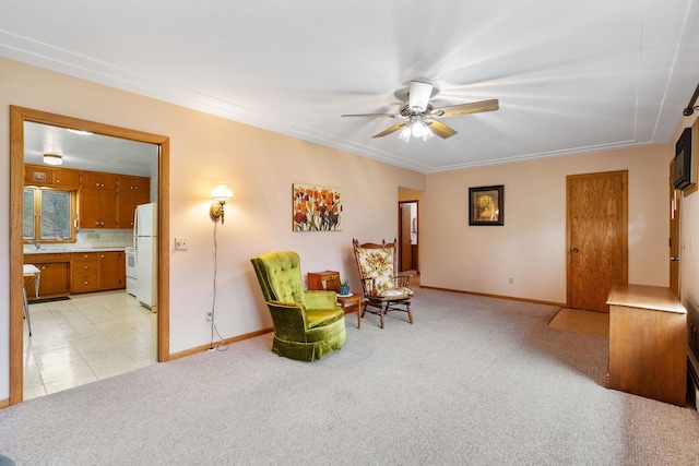 living area featuring crown molding, baseboards, ceiling fan, and light colored carpet