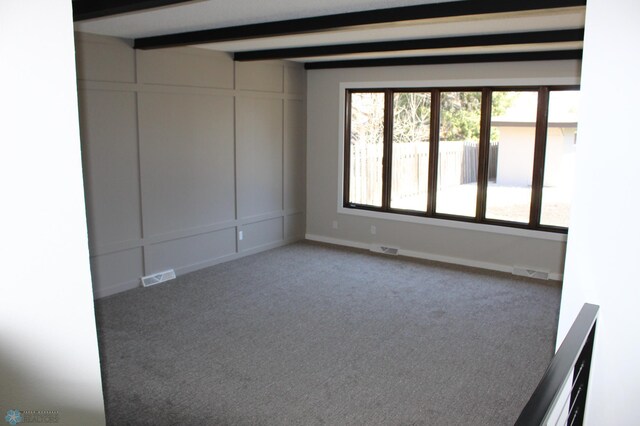 empty room featuring carpet floors, visible vents, and beam ceiling
