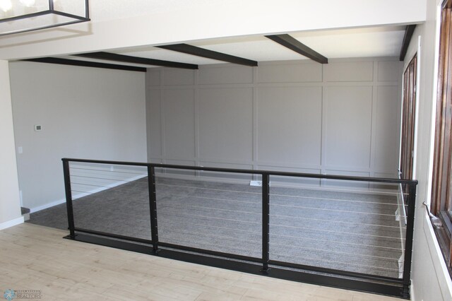 empty room featuring wood finished floors, beam ceiling, and a decorative wall