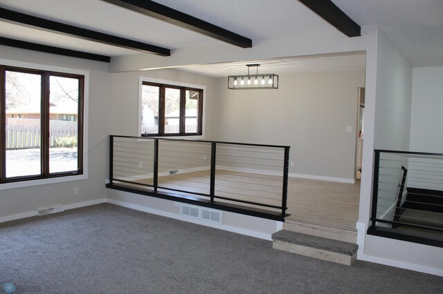 carpeted spare room featuring beamed ceiling, visible vents, and baseboards