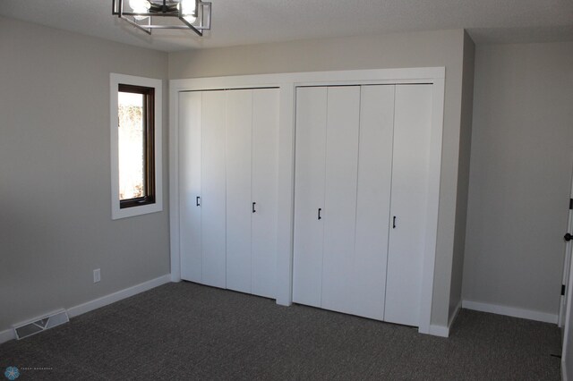 unfurnished bedroom featuring visible vents, baseboards, two closets, and dark colored carpet