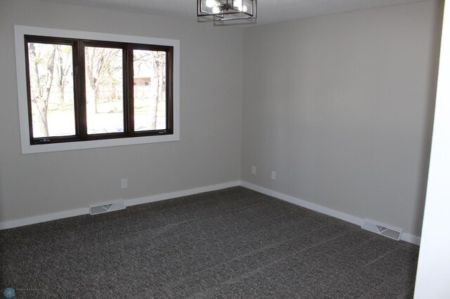 empty room with visible vents, dark carpet, and a chandelier