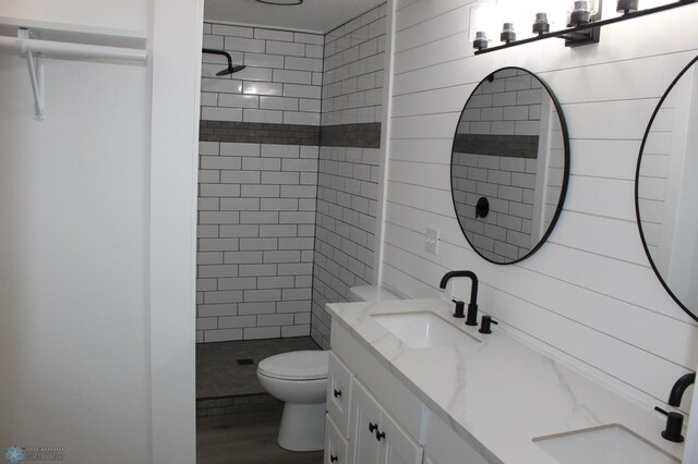 bathroom with vanity, wood finished floors, toilet, and tiled shower