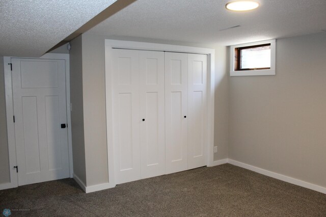 unfurnished bedroom with dark colored carpet, a textured ceiling, baseboards, and a closet