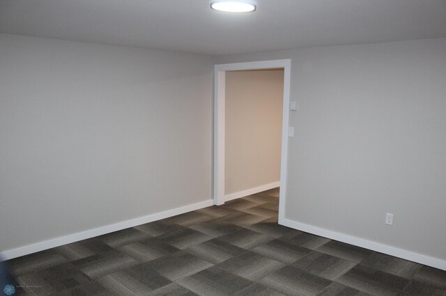 spare room with baseboards and dark colored carpet