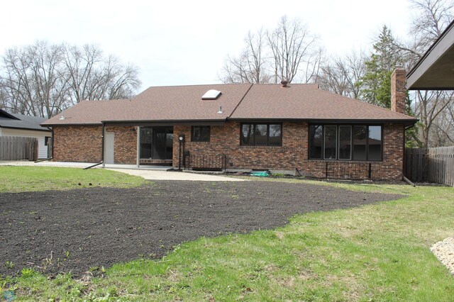 rear view of house with a chimney, roof with shingles, brick siding, fence, and a yard