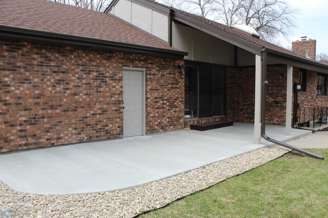 rear view of house with brick siding, a shingled roof, and a patio area