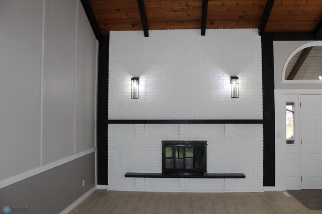 unfurnished living room with lofted ceiling with beams, wooden ceiling, wood finished floors, and a glass covered fireplace