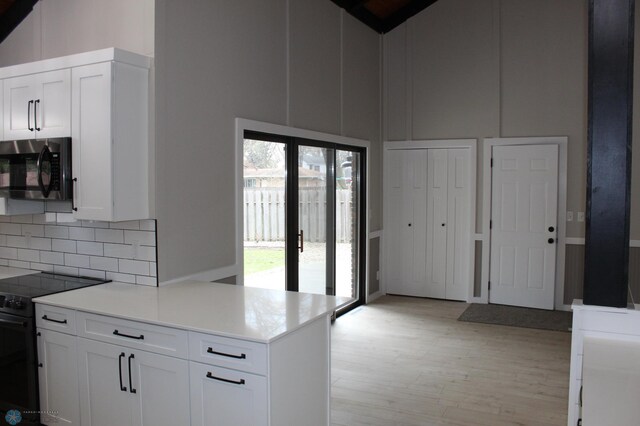 kitchen featuring light wood-style flooring, stainless steel microwave, high vaulted ceiling, and black range with electric stovetop