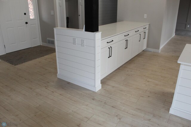 kitchen with a peninsula, baseboards, light countertops, white cabinets, and light wood-style flooring