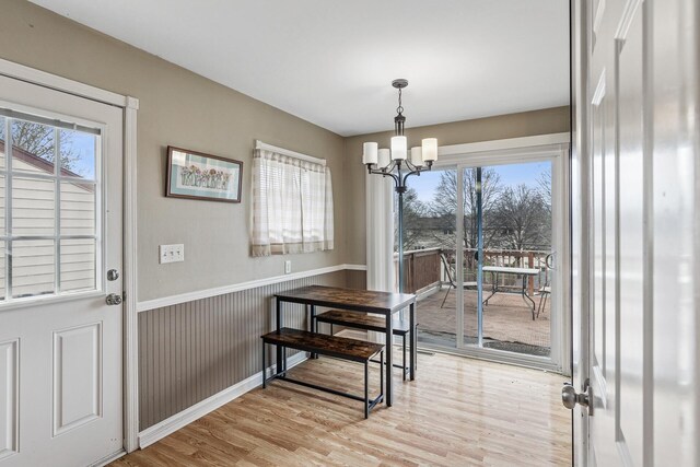 dining space featuring a chandelier, plenty of natural light, a wainscoted wall, and light wood-type flooring