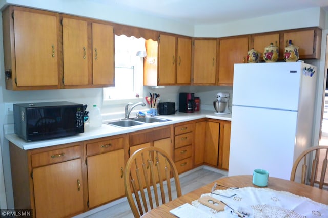 kitchen with a sink, freestanding refrigerator, brown cabinetry, light countertops, and black microwave