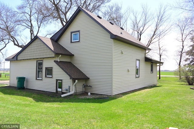 back of property with a shingled roof and a lawn