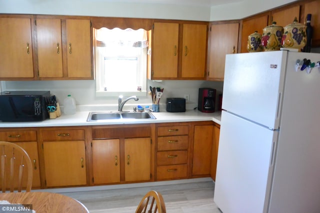 kitchen featuring freestanding refrigerator, a sink, black microwave, brown cabinets, and light countertops