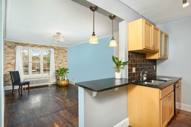 kitchen with dark countertops, a sink, baseboards, dishwashing machine, and radiator