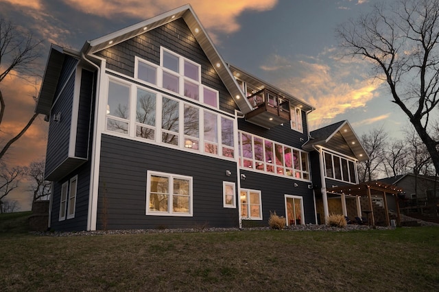 back of property at dusk featuring a yard, a sunroom, and a balcony