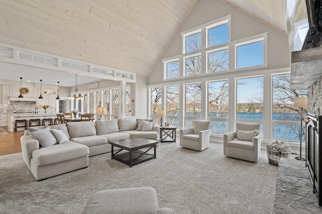 living room with a notable chandelier, carpet floors, high vaulted ceiling, wooden ceiling, and a water view
