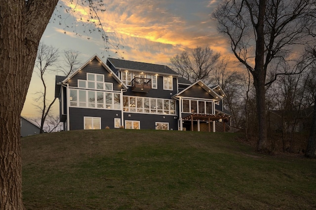 back of house at dusk featuring a lawn and a sunroom