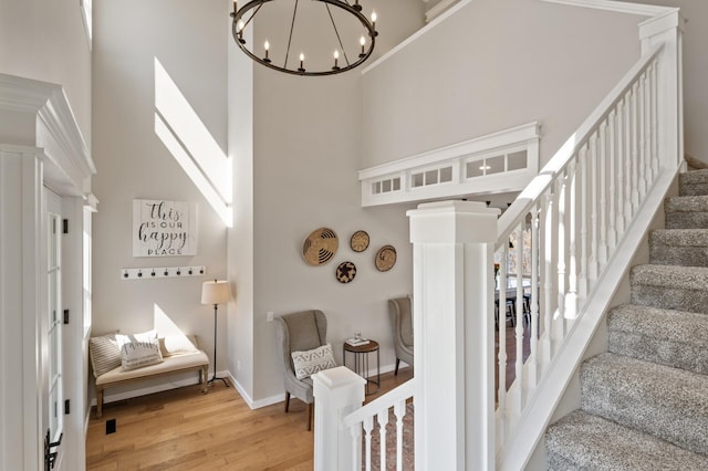 stairway with baseboards, a towering ceiling, wood finished floors, and a notable chandelier