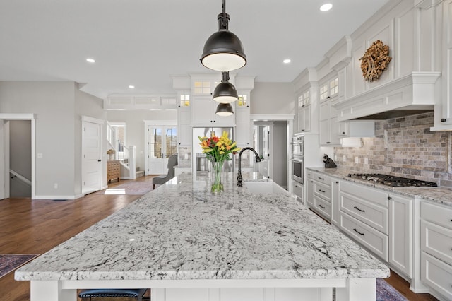 kitchen with white cabinets, appliances with stainless steel finishes, a sink, baseboards, and a large island