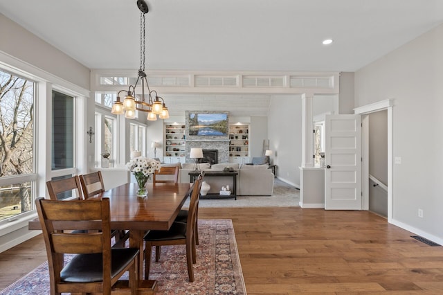 dining room with an inviting chandelier, baseboards, a large fireplace, and wood finished floors