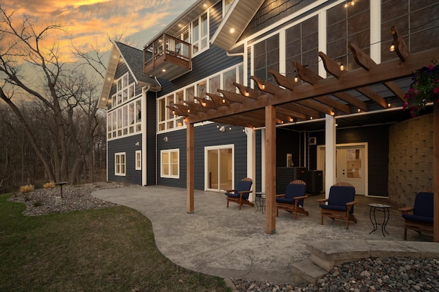 back of house at dusk with a pergola, a balcony, and a patio area