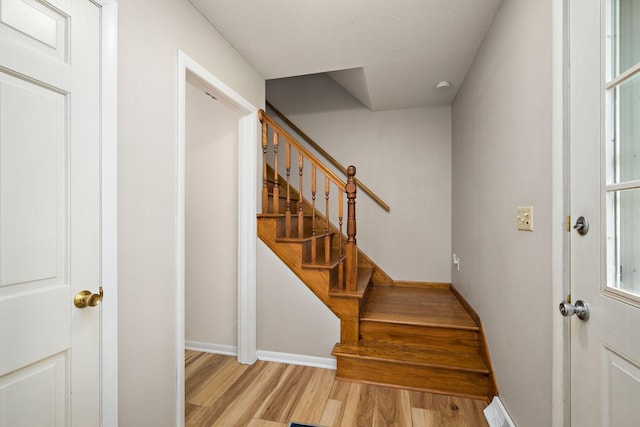 stairway featuring a textured ceiling, baseboards, and wood finished floors