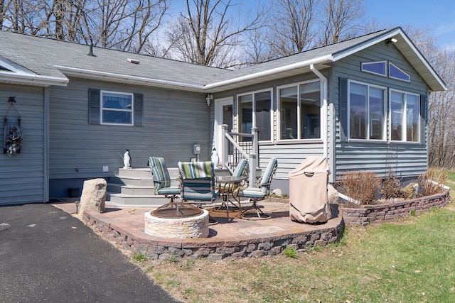 rear view of house featuring a patio area, a fire pit, a yard, a sunroom, and a shingled roof