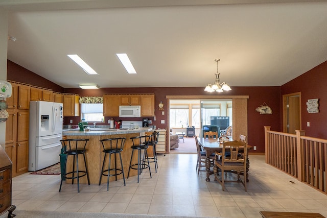 kitchen with lofted ceiling, white appliances, a breakfast bar area, a center island, and a notable chandelier