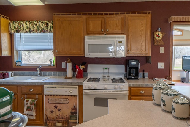 kitchen featuring light countertops, brown cabinetry, a sink, and white appliances