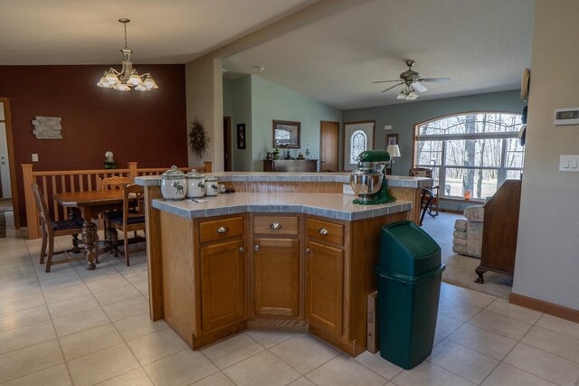 kitchen featuring ceiling fan with notable chandelier, brown cabinetry, pendant lighting, light countertops, and lofted ceiling
