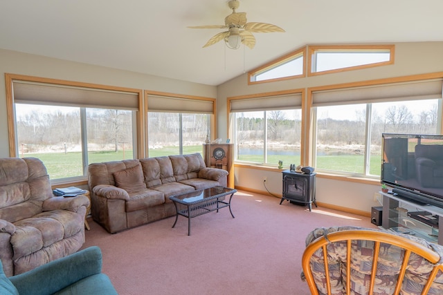 living room with a wood stove, vaulted ceiling, ceiling fan, carpet floors, and baseboards