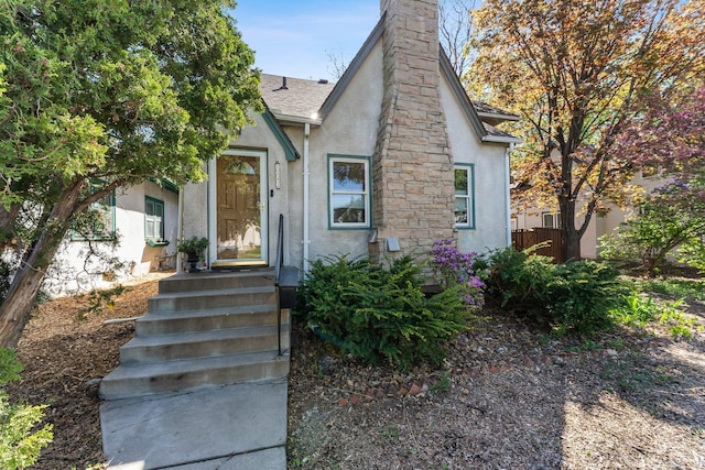 tudor home with stucco siding, fence, a chimney, and a shingled roof