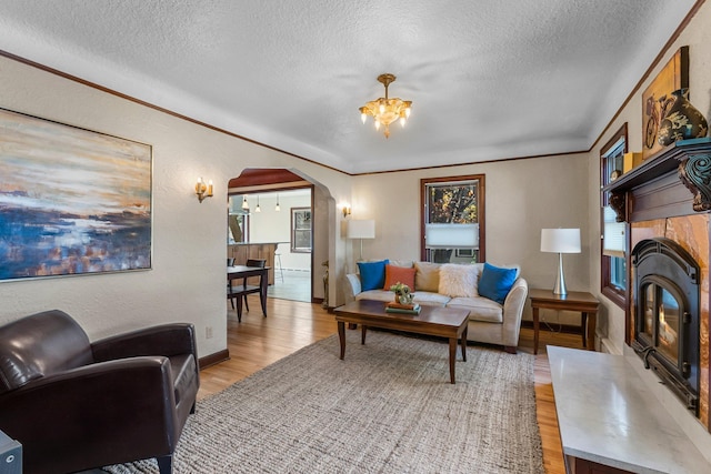 living area with a textured ceiling, a chandelier, light wood-type flooring, arched walkways, and plenty of natural light