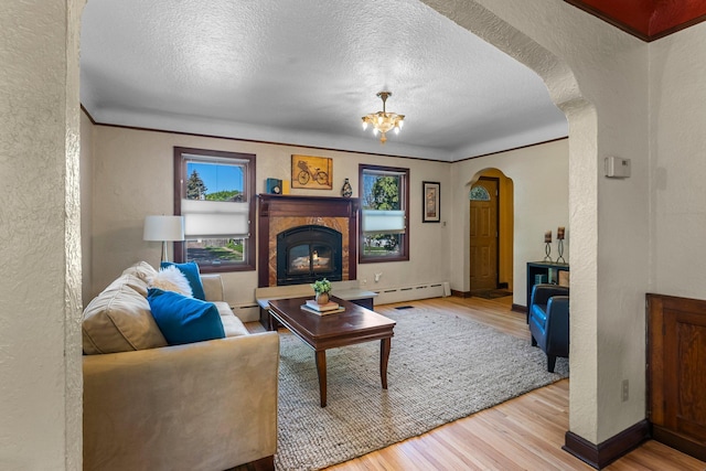 living room featuring a glass covered fireplace, a textured wall, arched walkways, wood finished floors, and a baseboard radiator