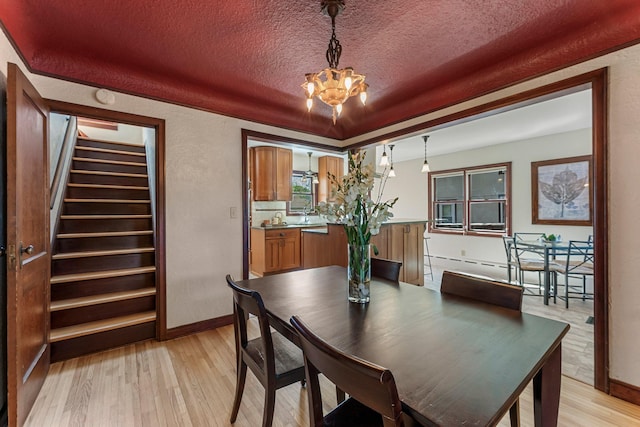 dining area with light wood-type flooring, a chandelier, a textured ceiling, stairway, and baseboards