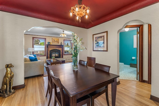 dining room with arched walkways, light wood finished floors, a glass covered fireplace, and a textured wall