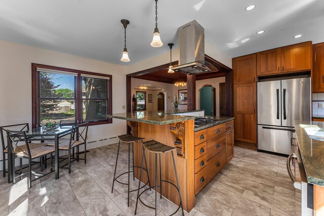 kitchen featuring stainless steel appliances, island range hood, brown cabinetry, arched walkways, and a kitchen bar
