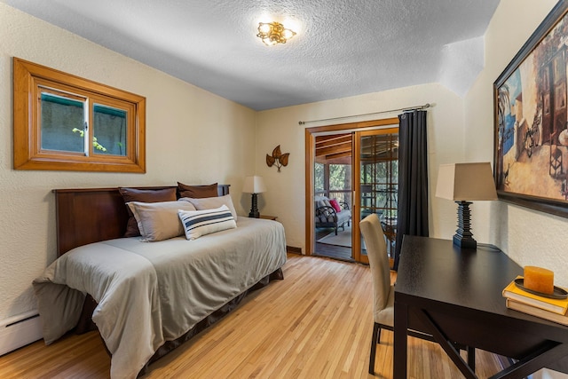 bedroom featuring access to exterior, light wood-style floors, a textured ceiling, a baseboard heating unit, and a textured wall