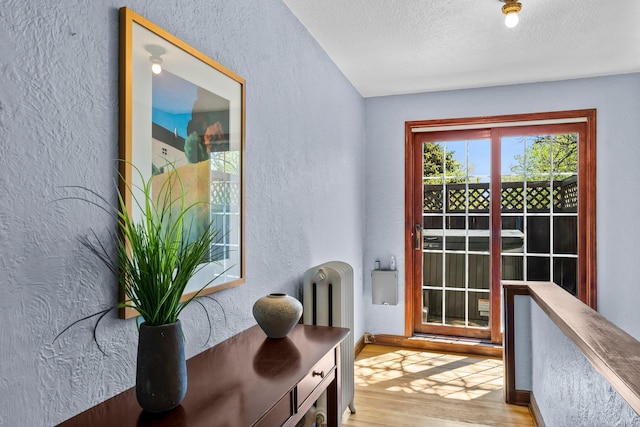 doorway with radiator heating unit, a textured wall, wood finished floors, a textured ceiling, and baseboards