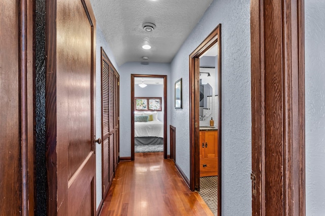 corridor with wood finished floors, a textured wall, a textured ceiling, and baseboards
