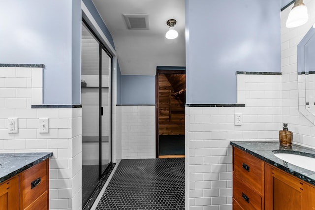 full bath featuring tile walls, a shower stall, vanity, wainscoting, and tile patterned floors