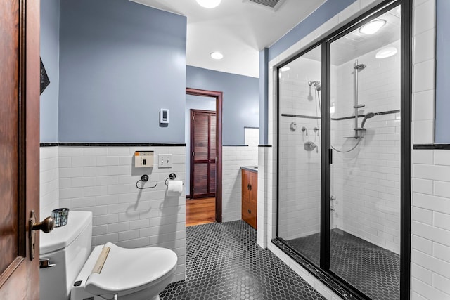 bathroom with tile walls, tile patterned flooring, a shower stall, a wainscoted wall, and toilet