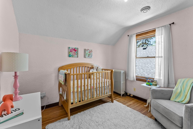 bedroom with lofted ceiling, a textured ceiling, wood finished floors, radiator, and a crib