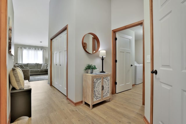 hallway with washer / clothes dryer, baseboards, and light wood-style floors