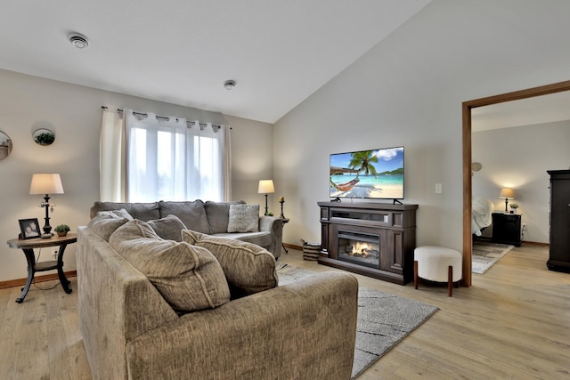 living area with light wood-type flooring, baseboards, a glass covered fireplace, and lofted ceiling